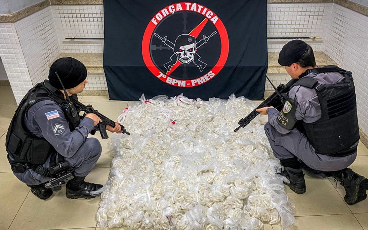 Dois Policiais Militares agachados, e no chão de delegacia 26 mil pinos de cocaina