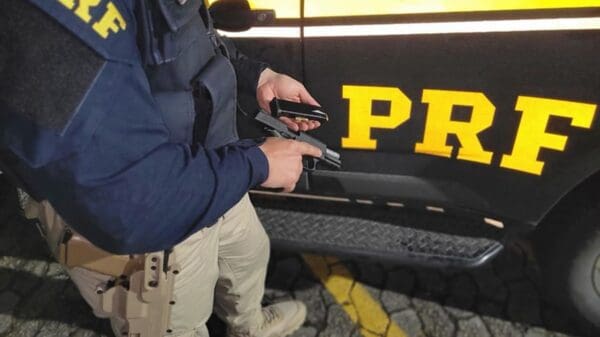 Agente da Polícia Rodoviária Federal segurando pistola 9mm, apreendida em fsicalização
