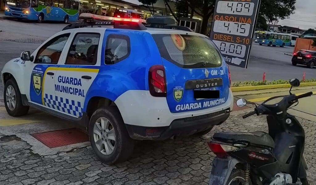 Viatura da Guarda Civil Municipal, ao lado da Moto, marca Honda modelo Bis, ao fundo o Terminal de ônibus de Carapina