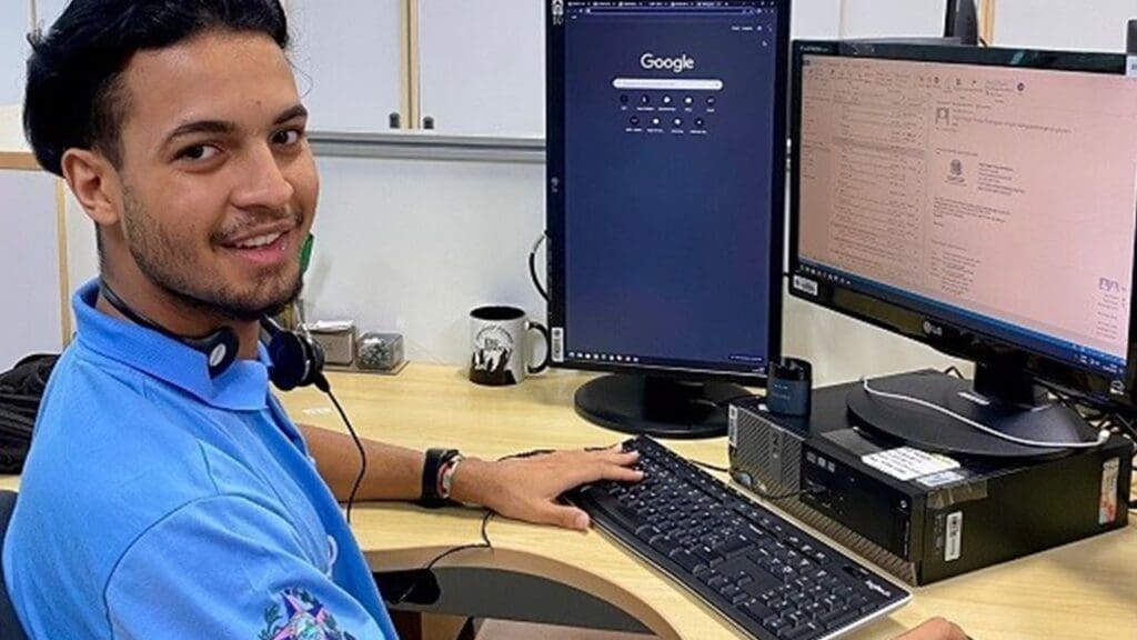 Foto de um estagiário sentado em frente de um computador sorridente