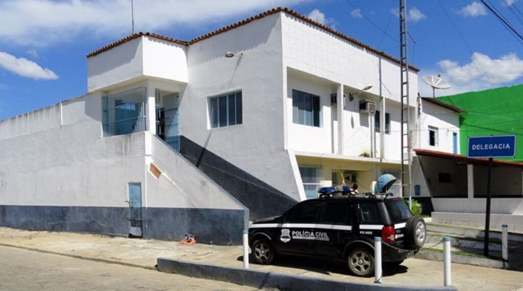 Foto da sede da Delegacia de Montanha (prédio de 2 andares, todo pintado de branco) em frente estacionada uma viatura e ao fundo um céu azul de um dia de calor