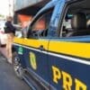Viatura da Polícia Rodoviária Federal estacionada e um agente fazendo abordagem a um motorista
