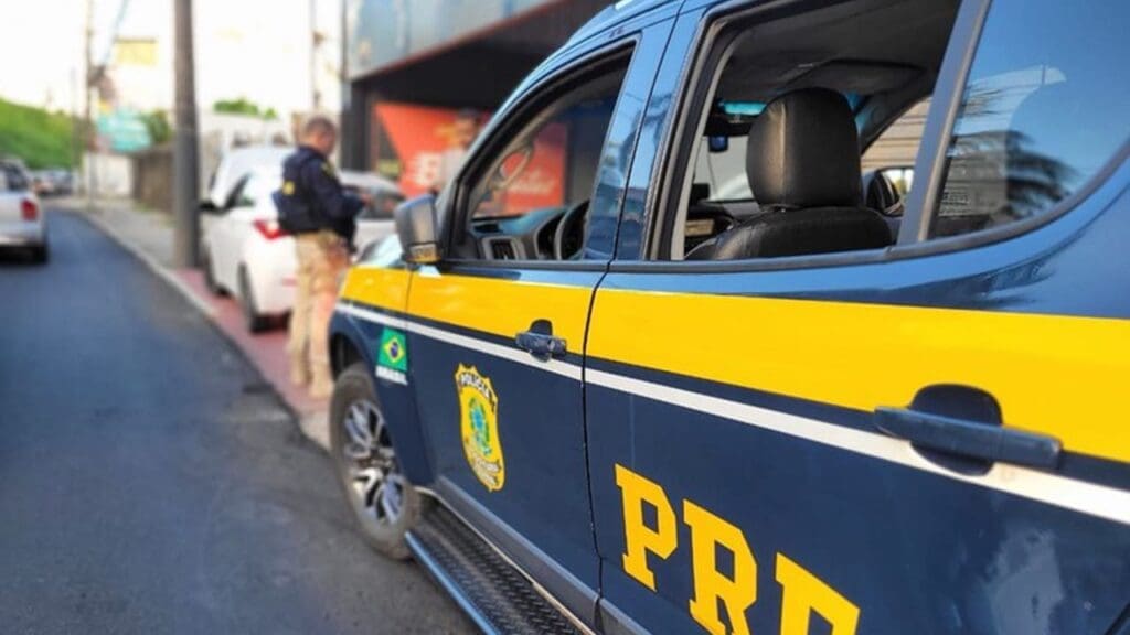 Viatura da Polícia Rodoviária Federal estacionada e um agente fazendo abordagem a um motorista