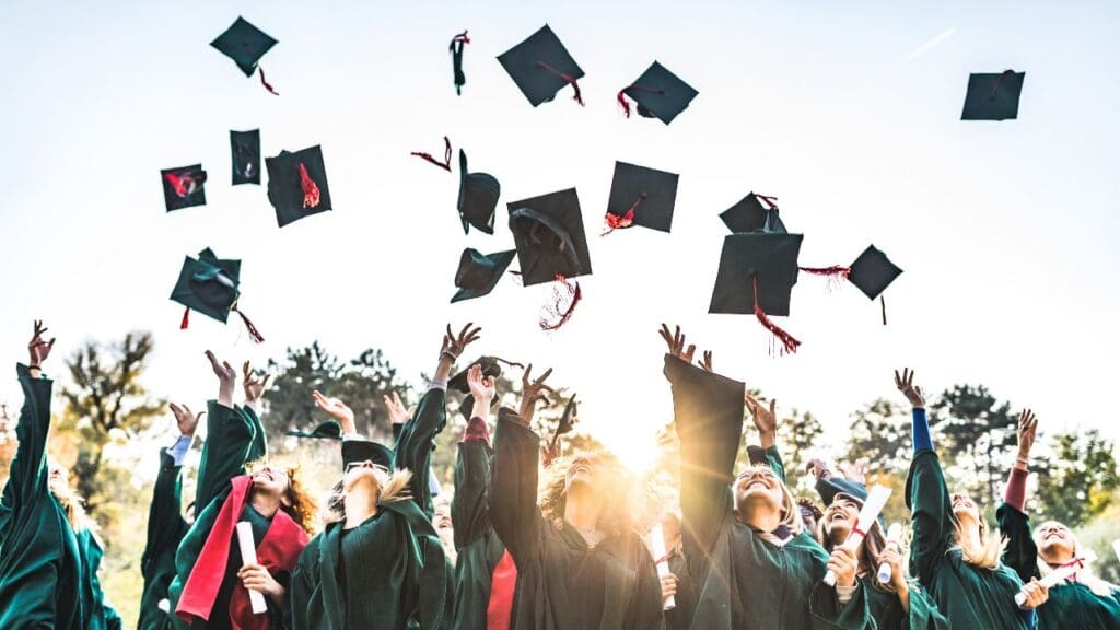 alunos comemorando vestidos com suas becas e jogando seus capelos para o alto (capelo)