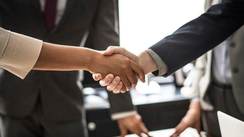 Em volta da mesa pesos de ternos e no centro da foto um aperto de mão entre duas pessoas simbolizando um acordo