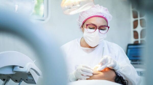Foto de uma Dentistante atendendo uma paciente que está com a boca aberta enquanto a doutora, realiza exames em sua boca