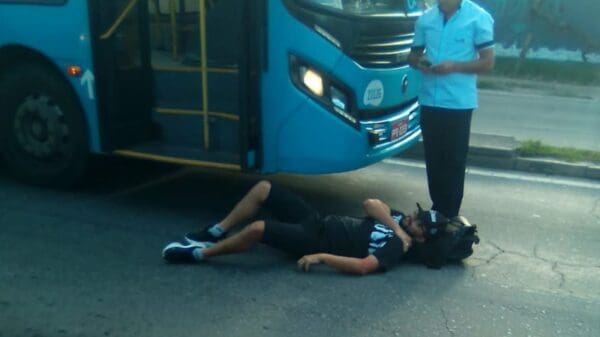 Homem caído no asfalto ao lado do ônibus