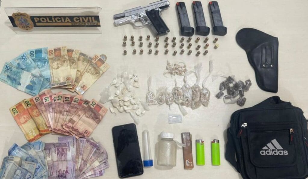 Foto divulgada pela polícia civil da apreensão realizada em Jaguare, sobre a uma mesa branca aproximadamente 670 reais em cedulas uma pistola cromada, 3 carregadores, 35 munições da pistolas intactas, 1 celular, porções de drogas embaladas para a venda, uma pochote, dois isqueiros