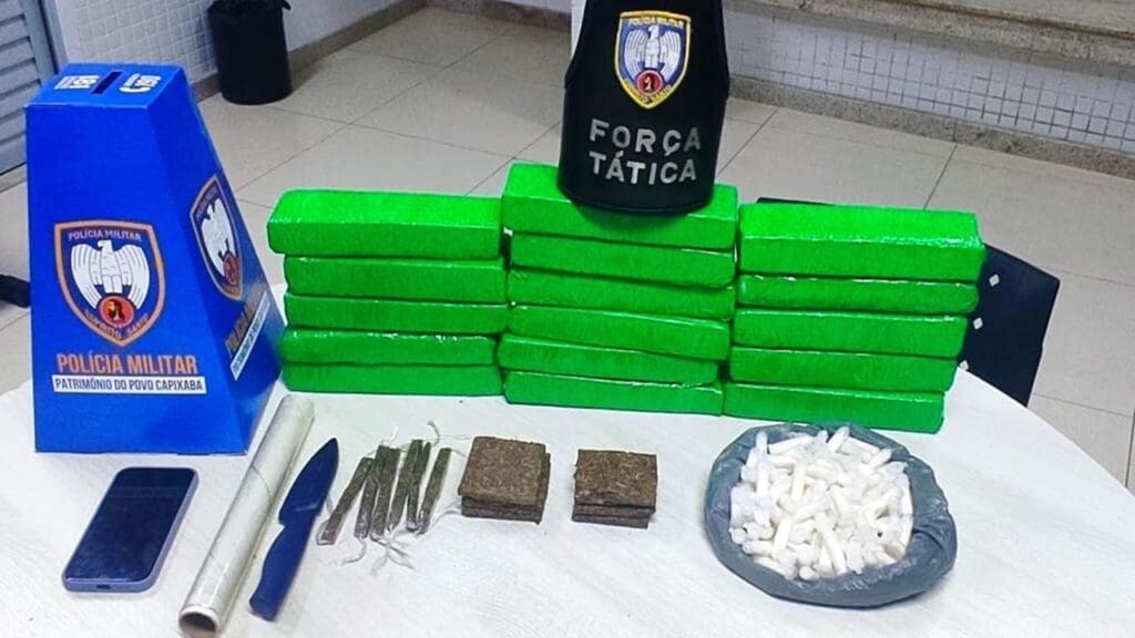 Sobre uma mesa branca 16 tabletes de maconha, além de seis palitos de maconha, 180g de maconha em pedaços, 170 pinos de cocaína, um celular e materiais para embalo.