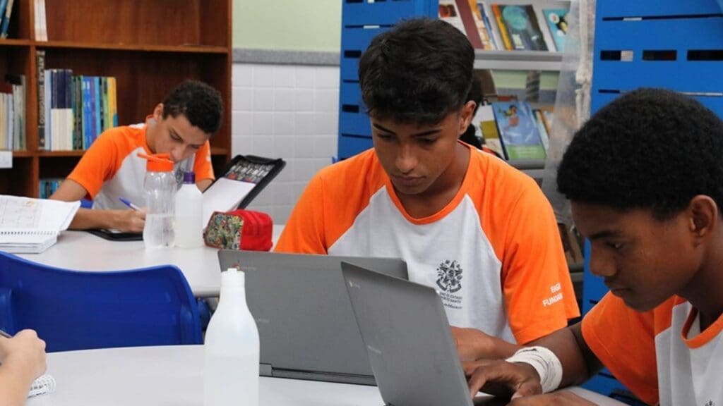 Foto em uma sala de aula três alunos estudando em seus notebook's