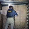 Foto de um agente da Polícia Federal dentro de um baú de caminhão, em frente a pilhas de caixas de cigarros que estava sendo contrabandeando