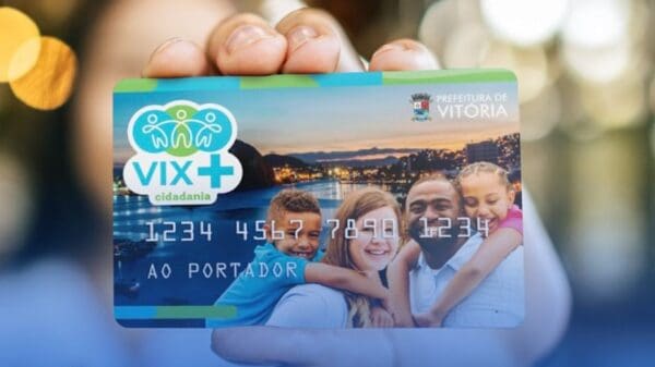 Imagem de uma mulher segurando o cartão alimentação do Programa da Prefeitura de Vitória Vix Mais Cidadania, e o fundo da foto esta desfocado