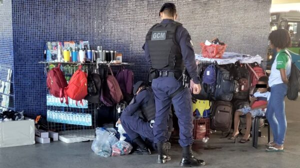 Foto do Terminal Jacaraípe, com uma barraca de ambulante e 2 agentes da GCM, vistoriando os produtos vendidos pelos ambulantes e ao lado uma mulher com as mãos para trás