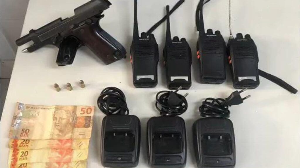 sobre uma mesa branca, uma pistola Taurus, com um carregador de 15 munições, três munições calibre 32, R$ 110 em espécie e uma bucha de maconha