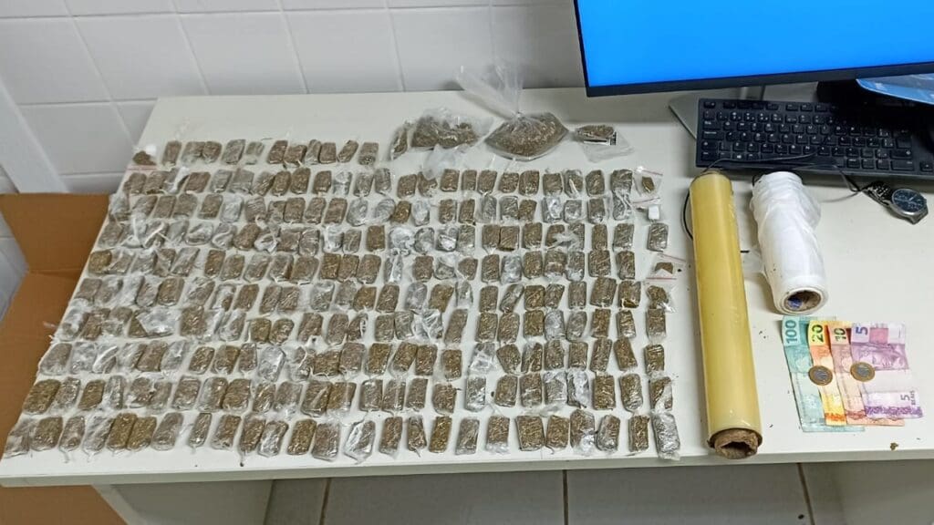 Foto sobre uma mesa 238 buchas de maconha, 3 sacos com maconha, pesando cerca de 51,6 gramas, além de material para embalo e R$ 137 em espécie.