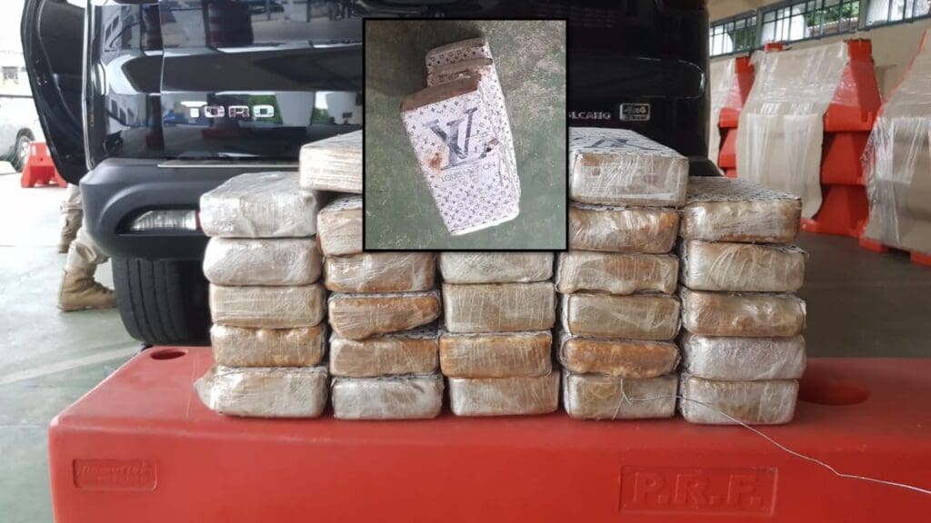 Foto imagem de 22 barras de pasta base de cocaína empilhadas, e no centro da imagem uma foto do bloco que esta embalada com a logo da Louis Vuitton