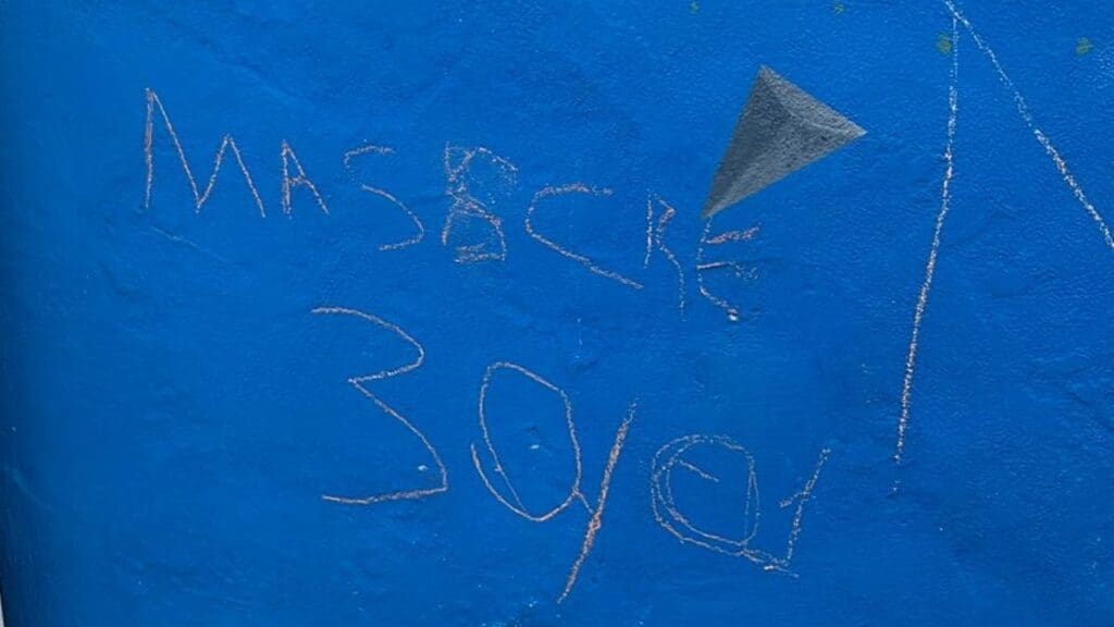 Foto de um muro azul riscado dom a tentativa de escrever "Massacre 30/01" mas está escrito "Masscre 30/01"