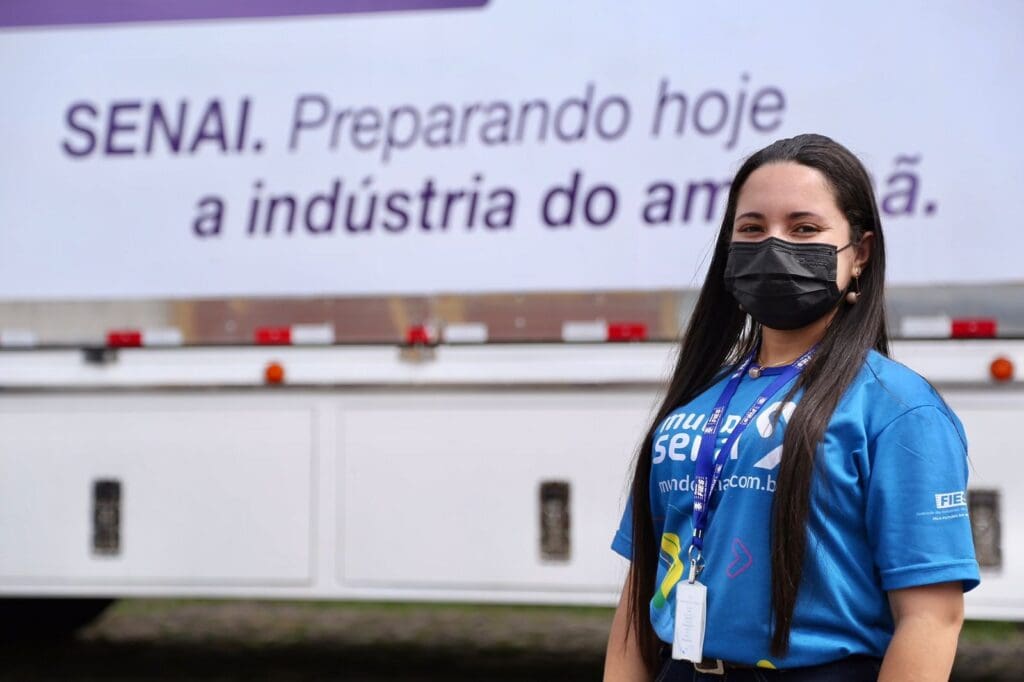 Mulher com uniforme do SENAI e ao fundo logo do SENAI