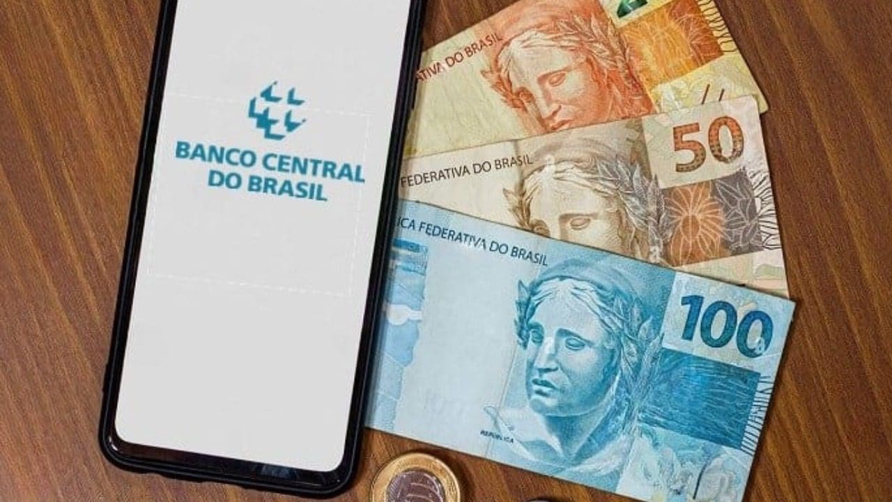 Foto de um celular aberto no site do Banco Central e dinheiro