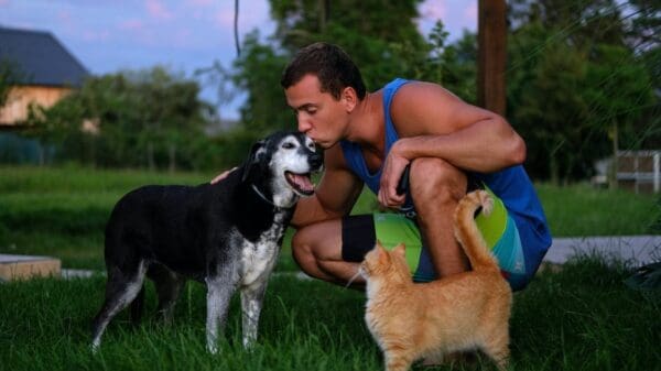 Homem beijando cachorro e gato ao lado