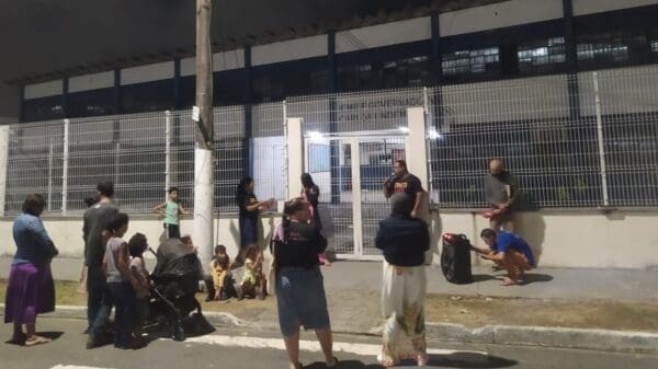 Um grupo de aproximadamente 20 pessoas em frente a uma escola na Serra, realizando um culto.