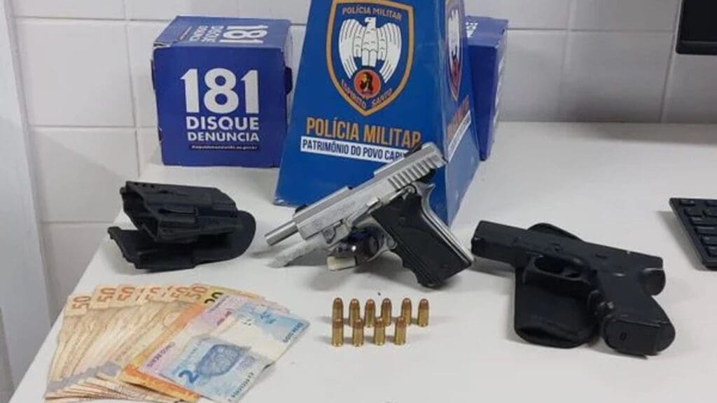 Sobre uma mesa branca uma pistola, uma arma falsa,10 munições além de R$ 427 em dinheiro