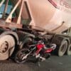 Foto com uma carreta estacionada ao lado de uma Moto Honda/XRE 300 vermelha com o pneu traseiro amassado após acidente fatal
