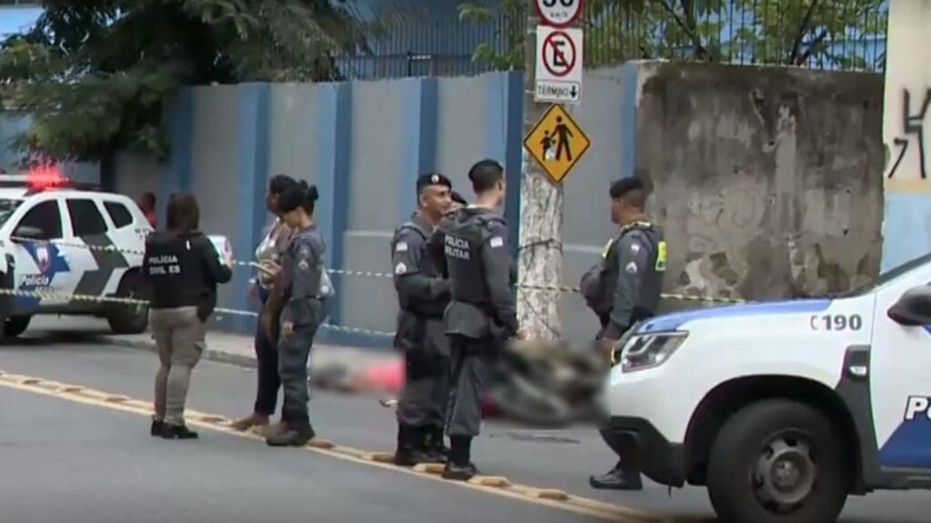 Foto em uma rua uma moto caída ao lado de um poste e os corpos do casal na pista, em volta da cena do crime 7 Policiais Militares registrando a ocorrência