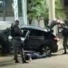 Foto dois Policiais Militares revistando um veículo, enquanto o motorista está no chão aguardando a revista