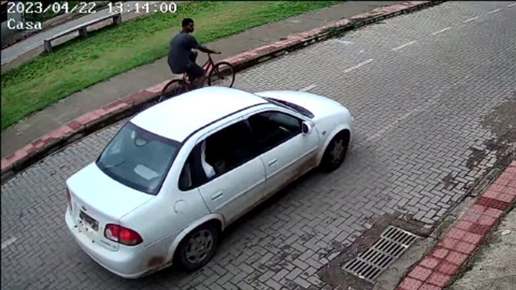 Foto um corsa branco e um homem de bicicleta passando em uma rua de paralelepippedo