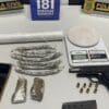 Foto sobre uma mesa uma pistola .380, 7 munições, um carregador, porções de maconha embaladas para venda, material para embalar drogas e uma balança de precisão.