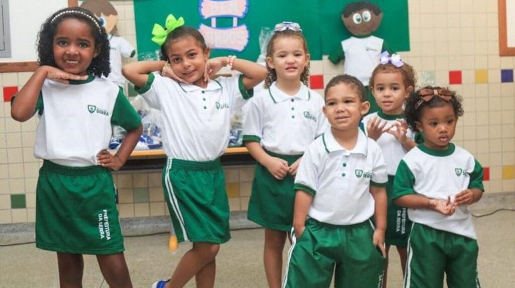 Foto de um grupo de 6 crianças vestidas com os novos uniformes escolares fazendo pose para a foto da divulgação do kit escolar