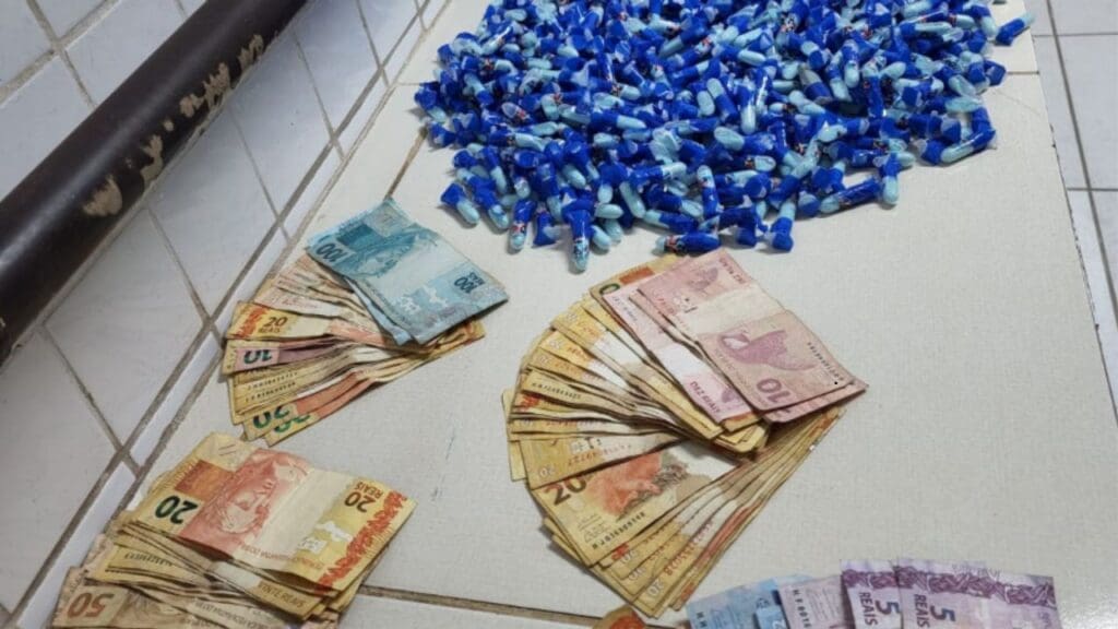 Sobre um banco 1.374 pinos de cocaína, 1 sacola contendo cocaína com peso de 445 gramas, 22 papelotes de raxixe, R$ 3.944 reais em espécie, 3 balanças de precisão, 1 munição calibre .380 e material de embalo.