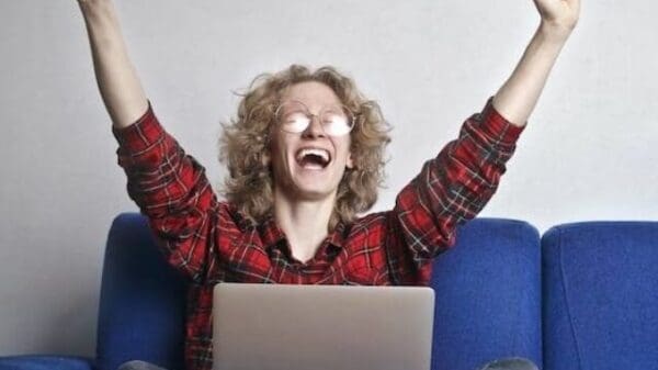 Mulher sentada no sofá com computador no colo e comemorando