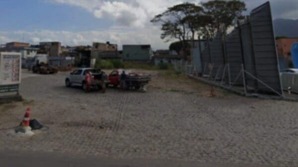 Foto de terreno com piso de paralelepípedo próximo ao bairro José de Anchieta na BR-110 na cidade da Serra, no local há duas camionetes estacionadas e pessoas paradas em volta.