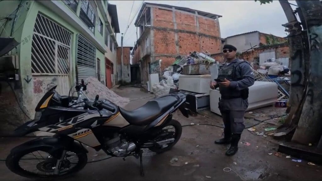 Foto do Cabo Marques da Policia Militar em um beco ao lado de uma motocicleta com restrição de furto/roubo