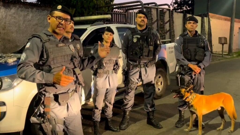 Foto do Sargento Mauricio Sousa apresentando outros 4 policiais militares que estão parados em frente a uma viatura da Policia Militar e junto com os militares o cão farejador Apollo.