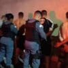 Polícia Militar prendendo 5 sujeitos encostados em um muro, todos os sujeitos estão com as mãos para trás enquanto são algemados pela PM