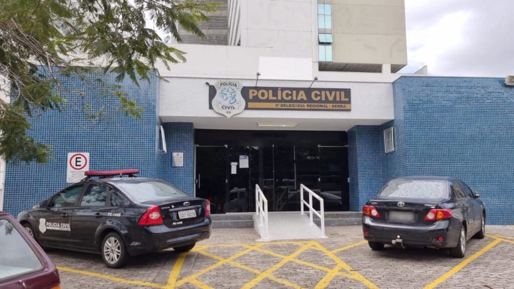 Foto da entrada da 3ª Delegacia Regional da Serra, com dois veículos estacionados no patio da Delegacia.