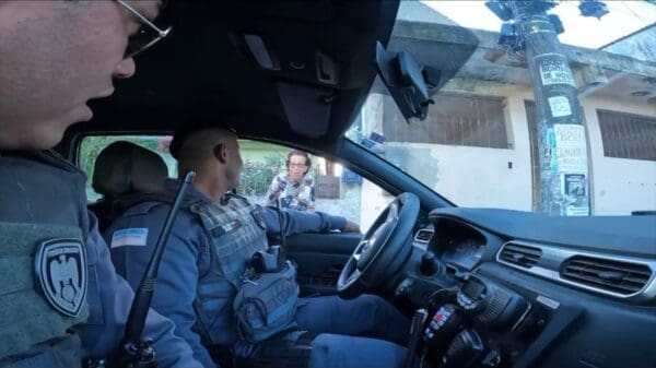 Imagem de dentro da viatura onde é possível ver dois policiais militares conversando com uma simpática senhora, que estava chapiscando o muro de sua residência