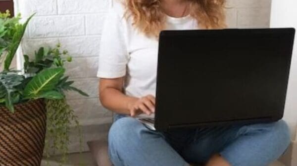 Mulher usando fone e assistindo em computador que está sobre o colo