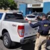 Foto de uma caminhonete estacionada no patio da 3ª Delegacia Regional da Serra, com um agente da PRF proximo a caçamba do veículo.