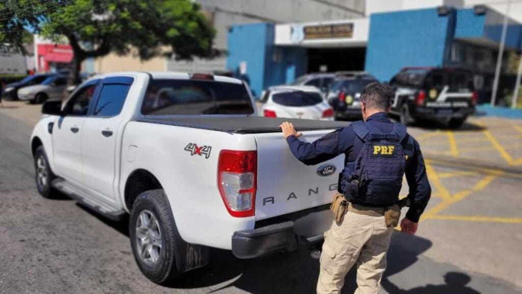 Foto de uma caminhonete estacionada no patio da 3ª Delegacia Regional da Serra, com um agente da PRF proximo a caçamba do veículo.