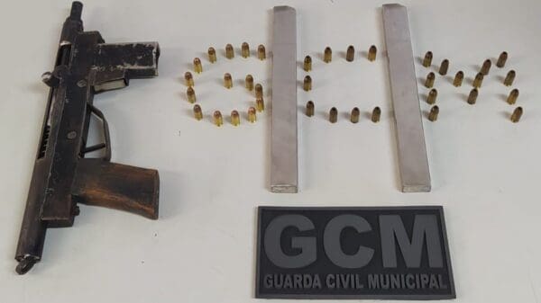 Sobre uma mesa branca uma submetralhadora, grafitada pelo crime, dois carregadores alongados além de 17 munições.