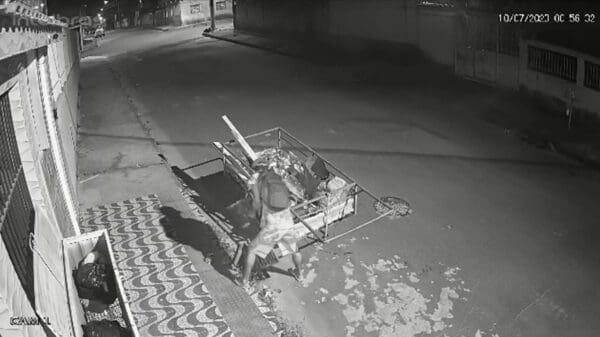 Imagem de uma câmera de segurança flagrando um homem (catador de materiais recicláveis), furtando uma grelha de proteção da rede fluvial de em uma rua residencial, sem movimento durante a madrugada