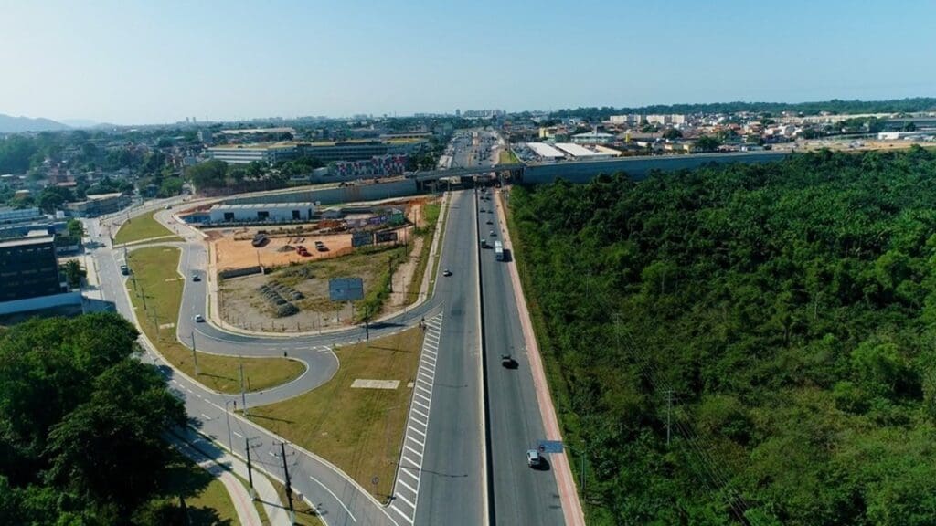 Vista aerea do Complexo Viário de Carapina, uma rodovia com uma mata verde do lado direito e algumas saidas da rodovia ao lado esquerdo, mais a frente o viaduto ainda em obras passando sobre a rodovia.