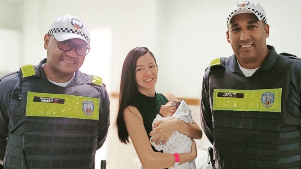 Foto de dois militares da BPTran ao lado de uma jovem mulher segurando um bebe de apenas 18 dias de vida, salvo pelos militares no momento que se engasgava