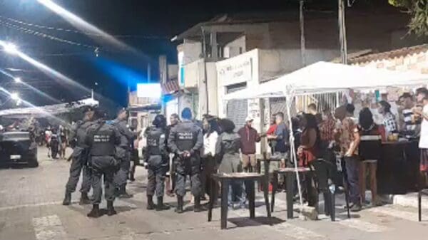Foto de uma equipe da Polícia Militar, em uma rua proximo a uma tenda conversando com realizadores de uma festa clandestina.
