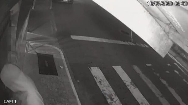 Foto de imagem de camera de segurança com um homem ateando fogo, em uma lixeira de uma rua deserta.
