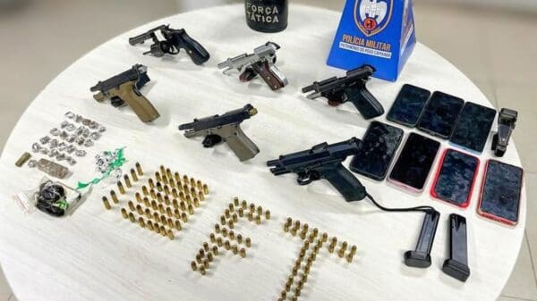 Sobre uma mesa redonda, um revólver calibre .38, 5 pistolas, 7 celulares, dezenas de munições e drogas.